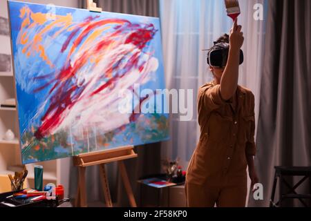 Peintre talentueux avec casque vr, représentant un chef-d'œuvre sur toile dans un studio d'art. Peinture d'art moderne sur toile, art créatif, contemporain et réussi dessin d'artiste chef-d'œuvre Banque D'Images