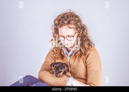 Détail d'une belle femme avec des lunettes et des cheveux bruns, assis souriant avec un chiot Jack Russel Terrier dans ses bras. De couleur rétro et vintage Banque D'Images