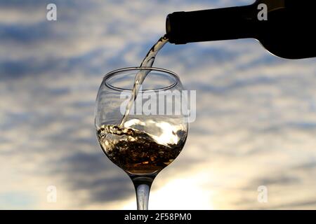 Vin blanc versé d'une bouteille dans le verre sur un magnifique fond de coucher de soleil. Concept de célébration, fête d'été à l'hôtel, dîner romantique Banque D'Images