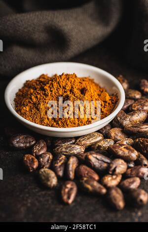 Poudre de cacao et fèves de cacao dans un bol sur table noire. Banque D'Images