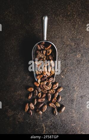 Fèves de cacao rôties dans une cuillère sur une table noire. Vue de dessus. Banque D'Images