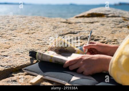 Femme se détendant sur la plage résoudre Crosswords pendant les vacances d'été. Banque D'Images