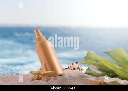 Bouteille de crème solaire sur une plage de sable décorée de différentes coquillages sur fond de vagues de mer. Banque D'Images