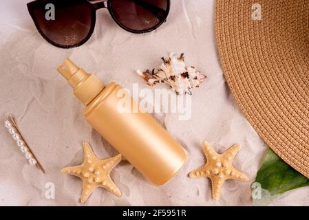 Bouteille de crème solaire sur une plage de sable décorée de différentes coquillages sur fond de vagues de mer. Banque D'Images