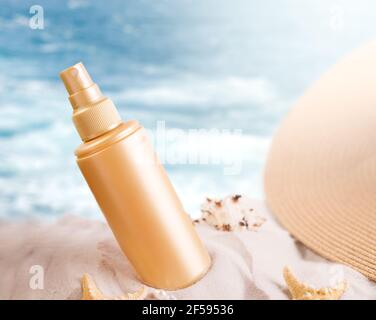 Bouteille de crème solaire sur une plage de sable décorée de différentes coquillages sur fond de vagues de mer. Banque D'Images