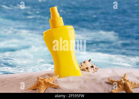 Bouteille de crème solaire sur une plage de sable décorée de différentes coquillages sur fond de vagues de mer. Banque D'Images