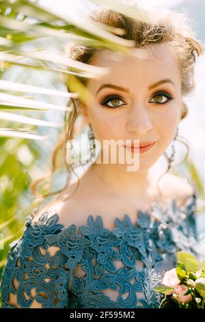 Portrait d'une mariée dans une élégante robe bleue avec un bouquet dans ses mains près des branches vertes de un treeclose-up Banque D'Images