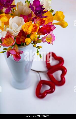 FREESIA dans un vase et coeur rouge sur fond blanc en bois. Banque D'Images