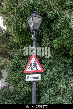 Panneau d'école triangle rouge et blanc avec les enfants tenant les mains sur un lampadaire lumineux de rue orné. Banque D'Images