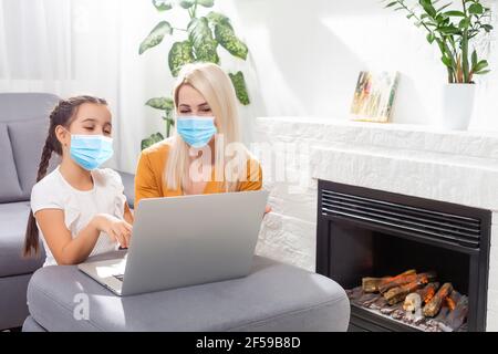 Coronavirus. Maman et fille portant un masque de protection en quarantaine. Restez à la maison, femme travaillant sur un ordinateur portable tout en prenant soin de bébé. Travail indépendant Banque D'Images