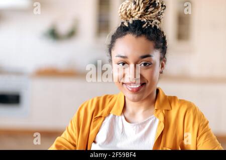 Portrait en gros plan de la jolie jeune femme afro-américaine heureuse avec des dreadlocks, freelance ou étudiante, vêtue de vêtements décontractés élégants, regarde directement l'appareil photo avec un sourire amical Banque D'Images