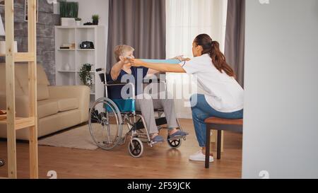 Femme âgée en fauteuil roulant en réadaptation avec bande de résistance. Formation, sport, récupération et levage, maison de retraite pour personnes âgées, soins infirmiers de santé, soutien de santé, aide sociale, médecin et service à domicile Banque D'Images