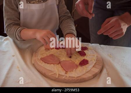 La main met les ingrédients sur une rangée de pizza sur un bois planche à découper Banque D'Images