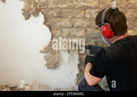 ouvrier retirant le plâtre du mur de briques intérieur avec le foret sds Banque D'Images