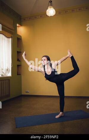 Femme attirante en noir pleine longueur vêtements de sport pratiquant le yoga en studio exécutant l'exercice natarajasana, roi des danseurs pose. Banque D'Images