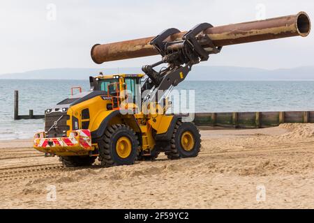 Volvo L180H Optishift Wheel Loader transportant de gros tuyaux le long de la plage pour les travaux de réapprovisionnement de plage à Bournemouth et Poole Beaches, Dorset UK en mars Banque D'Images