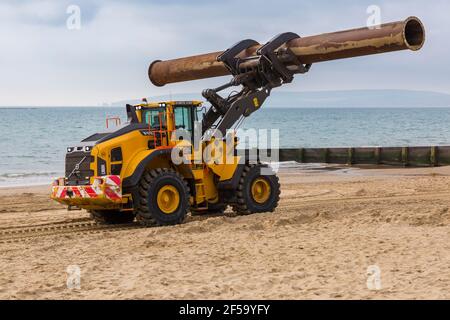 Volvo L180H Optishift Wheel Loader transportant de gros tuyaux le long de la plage pour les travaux de réapprovisionnement de plage à Bournemouth et Poole Beaches, Dorset UK en mars Banque D'Images