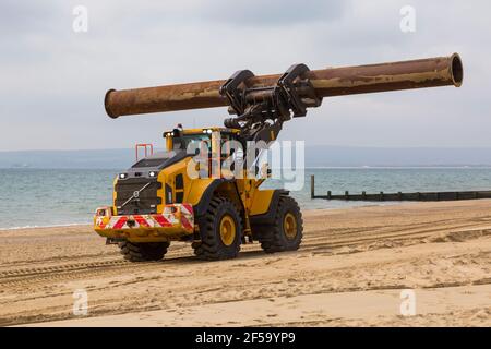 Volvo L180H Optishift Wheel Loader transportant de gros tuyaux le long de la plage pour les travaux de réapprovisionnement de plage à Bournemouth et Poole Beaches, Dorset UK en mars Banque D'Images