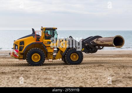 Volvo L180H Optishift Wheel Loader transportant de gros tuyaux le long de la plage pour les travaux de réapprovisionnement de plage à Bournemouth et Poole Beaches, Dorset UK en mars Banque D'Images