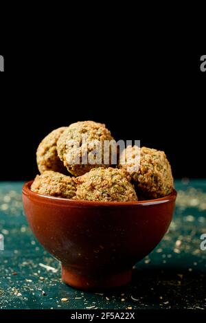 un peu de falafel dans un bol en faïence, sur une table rustique en bois vert, sur fond noir Banque D'Images