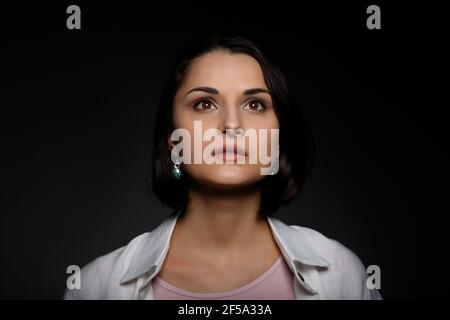 Portrait-clé bas de la jeune femme pluriethnique brunette sérieuse en débardeur rose et chemise blanche regardant vers le haut. Banque D'Images