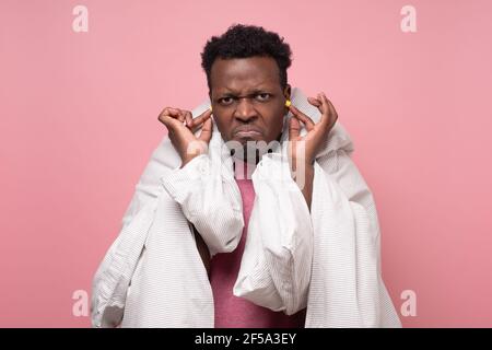 Un jeune homme de stress africain a inséré un bouchon d'oreille dans son oreille pour la protection contre le bruit. Prise de vue en studio Banque D'Images