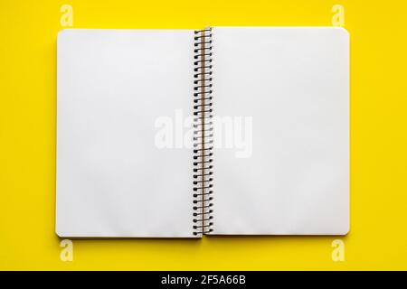 Cahier spirale ouvert avec feuilles blanches vierges sur fond jaune vif, vue de dessus, plat Banque D'Images