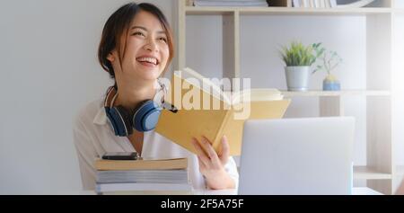 Portrait de la jeune fille asiatique souriante et de la lecture d'un livre à la maison avant d'apprendre virtuel Internet en ligne classe. Pandémie Covid. Banque D'Images