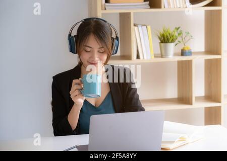 Portrait d'une fille étudiante asiatique souriante et de boire du café à la maison avant d'apprendre le cours virtuel en ligne sur Internet. Pandémie Covid. Banque D'Images