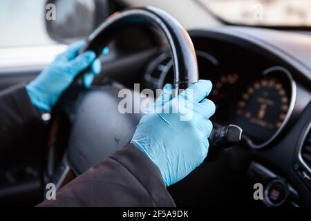 Les mains du conducteur portant des gants en caoutchouc bleu tenant le volant du véhicule, vue rapprochée Banque D'Images
