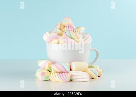 Guimauves de bonbons à la mode colorés dans une tasse sur fond bleu. Concept de nourriture de vacances sucrée. Banque D'Images