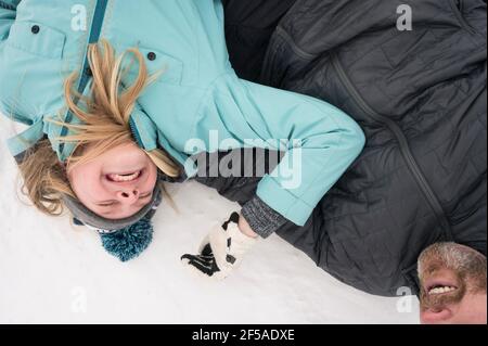 Père et fille riant couché dans la neige après Luge Banque D'Images