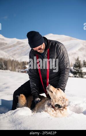 Homme jouant avec Golden Retriever Dog dans Snow on Sunny Jour Banque D'Images