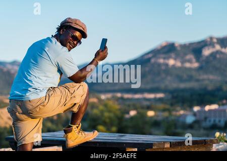 homme afro-américain avec un chapeau souriant regardant son mobile téléphone Banque D'Images