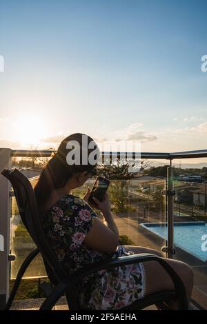 Femme méconnaissable prenant une photo du coucher de soleil dans un balcon Banque D'Images