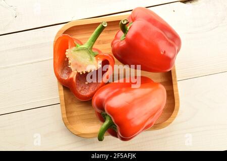 Deux poivrons rouges entiers et un demi sur une plaque de bambou, gros plan, sur une table en bois. Banque D'Images