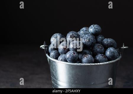 Myrtille fraîche et mûre dans un petit seau en métal sur fond noir. Baies de bleuets juteuses pleines de vitamines. Banque D'Images