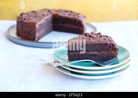 Une tranche ou une portion de gâteau au chocolat riche et humide fait maison sur une assiette. La tranche de gâteau a une garniture de crème au chocolat et une épaisse garniture au chocolat Banque D'Images