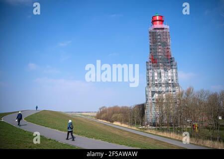 24 mars 2021, Basse-Saxe, Krumhörn: Les marcheurs passent devant le phare de Campener. Le phare le plus haut d'Allemagne est en cours de rénovation. Photo: Sina Schuldt/dpa Banque D'Images