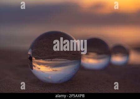 Trois boules de cristal claires de trois tailles sont sphérique révèle vue paysage avec sphérique placé sur le sable à Karon Beach pendant le coucher du soleil. Banque D'Images