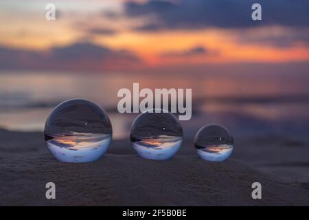 Trois boules de cristal claires de trois tailles sont sphérique révèle vue paysage avec sphérique placé sur le sable à Karon Beach pendant le coucher du soleil. Banque D'Images