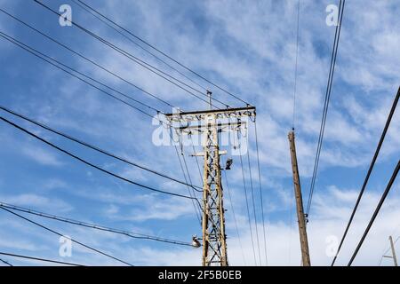 Ancienne tour de ligne électrique industrielle en métal rouillé à côté d'un poteau électrique traditionnel en bois placé contre un ciel bleu, aspect horizontal Banque D'Images