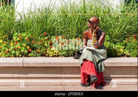 Chicago, Illinois, États-Unis - 15 août 2014 : jeune femme africaine à la peau sombre assise et à l'écoute de la musique avec des écouteurs dans le parc. Banque D'Images