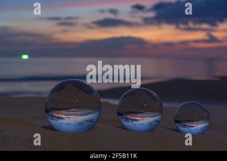 Trois boules de cristal claires de trois tailles sont sphérique révèle vue paysage avec sphérique placé sur le sable à Karon Beach pendant le coucher du soleil. Banque D'Images