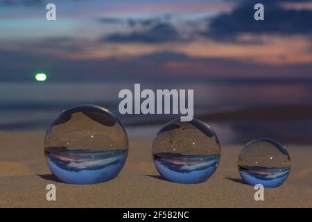 Trois boules de cristal claires de trois tailles sont sphérique révèle vue paysage avec sphérique placé sur le sable à Karon Beach pendant le coucher du soleil. Banque D'Images