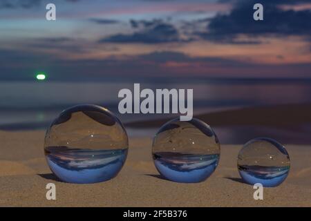 Trois boules de cristal claires de trois tailles sont sphérique révèle vue paysage avec sphérique placé sur le sable à Karon Beach pendant le coucher du soleil. Banque D'Images