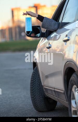 Femme tenant un nouveau masque médical dans sa main, étirant sa main à travers une fenêtre de voiture Banque D'Images
