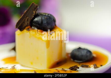 Une portion de cheesecake à la vanille décorée de bleuets et de morceaux de chocolat au lait, recouverte de sauce caramel, pause sucrée Banque D'Images