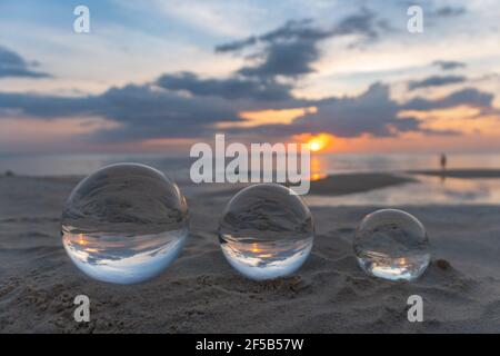 Trois boules de cristal claires de trois tailles sont sphérique révèle vue paysage avec sphérique placé sur le sable à Karon Beach pendant le coucher du soleil. Banque D'Images