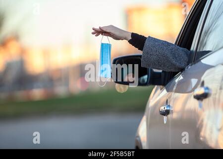 Une femme pilote jette un masque facial usagé à travers une fenêtre de voiture ou partage un nouveau transparent avec quelqu'un, l'espace de copie Banque D'Images